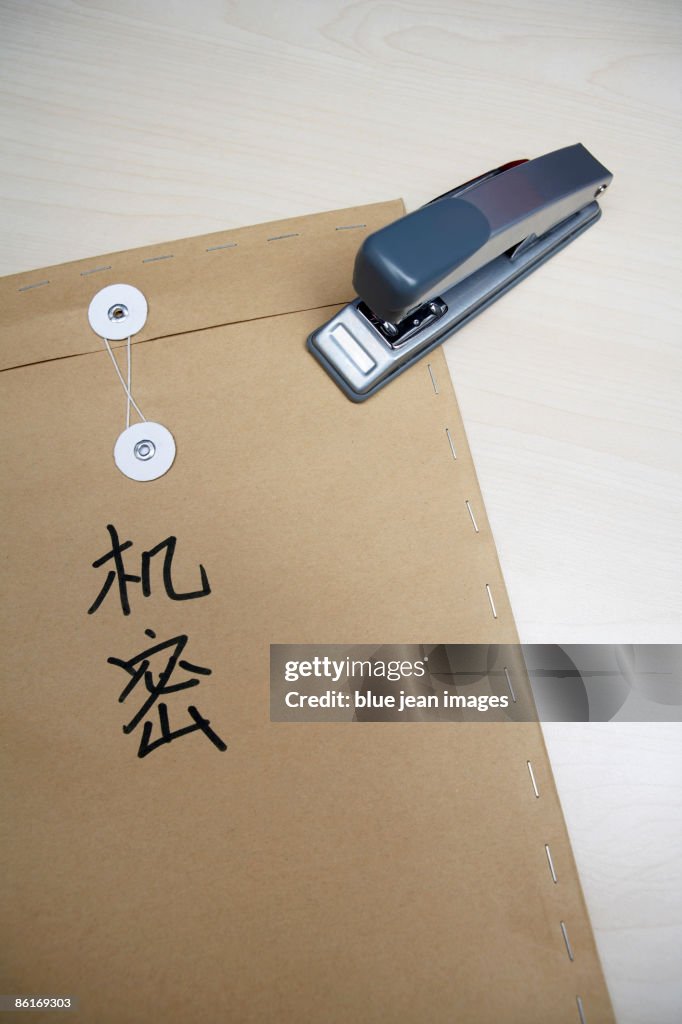 A stapler resting on a brown envelope that has 'top secret' in Chinese characters written on it
