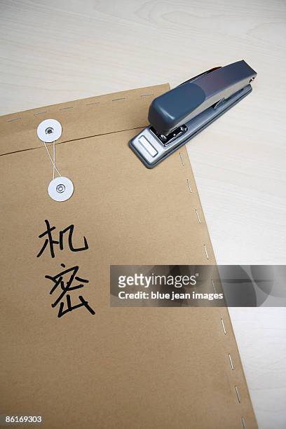 a stapler resting on a brown envelope that has 'top secret' in chinese characters written on it - manila envelope stock pictures, royalty-free photos & images