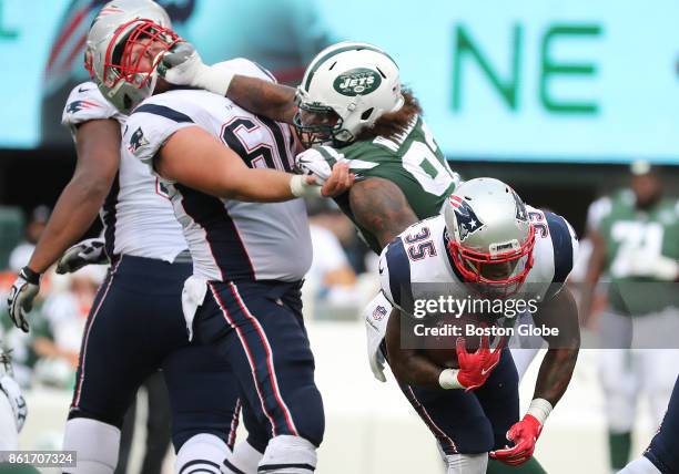 New England Patriots' Mike Gillislee runs with the ball as teammate Marcus Cannon gets a fist in the face from New York Jets' Leonard Williams during...