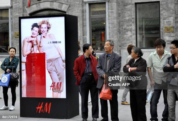 Chinese residents stand beside an advertising board for the new Hennes & Mauritz AB better known as H&M store, the international fashion retailer,...