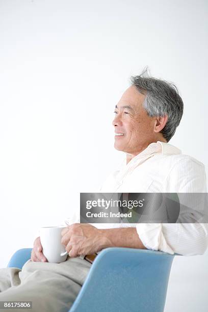 senior man sitting on armchair, holding coffee cup - hawaii hemd stock-fotos und bilder