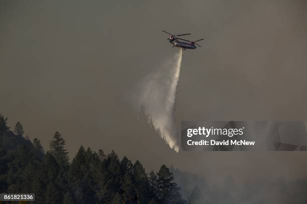 Firefighting helicopter drops water on the Tubbs Fire on October 15, 2017 near Santa Rosa, California. At least 40 people were killed with many are...