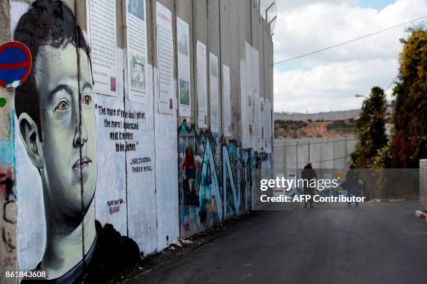 Two men walk past a new piece of graffiti depicting Chief Executive Officer and founder of Facebook Inc Mark Zuckerberg on the controversial Israeli...