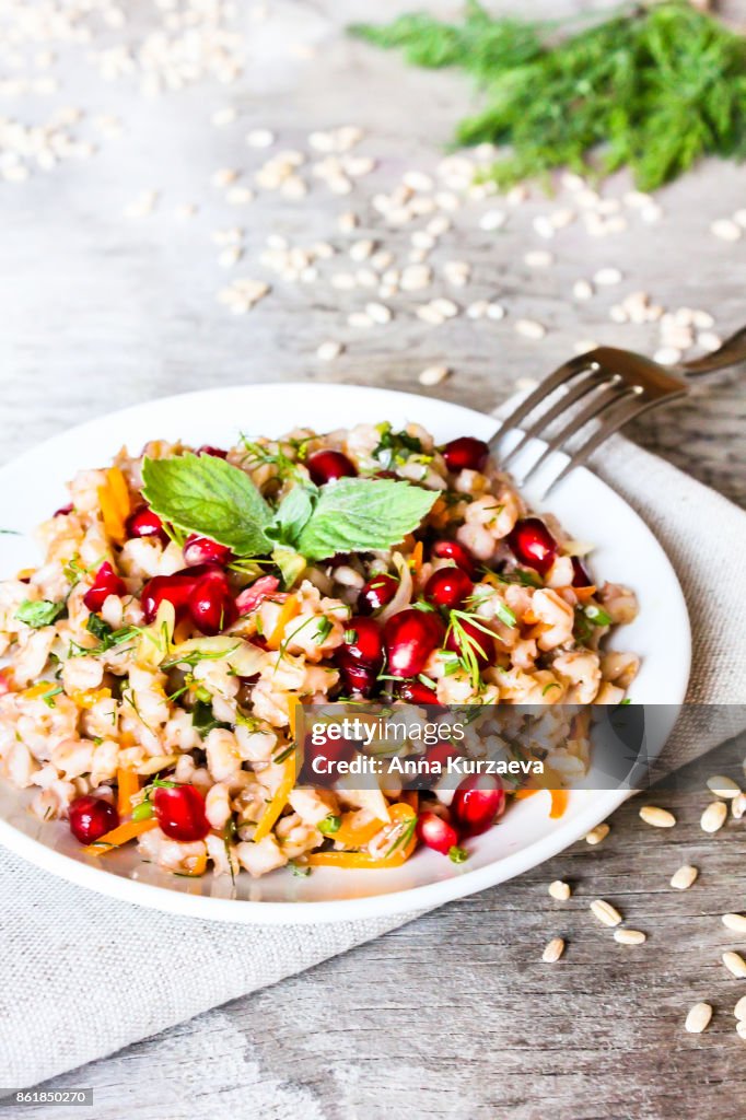 Warm salad with barley, carrot, onion, pomegranate seeds and fresh mint in a plate on a wooden table, selective focus