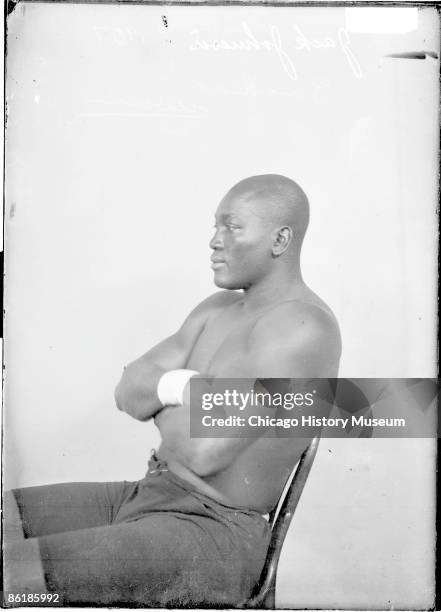 Three-quarter length portrait of Jack Johnson, African American heavyweight champion boxer, in profile, sitting in a chair in front of a light...