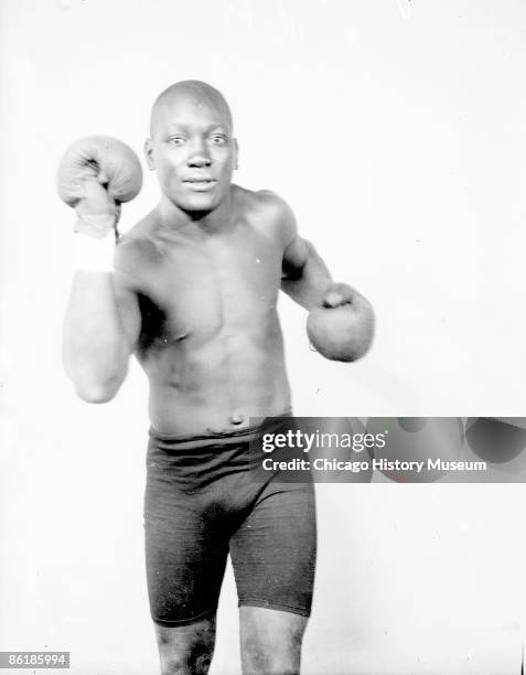 Three-quarter length portrait of Jack Johnson, African American heavyweight champion boxer, standing in front of a light colored background in a room...
