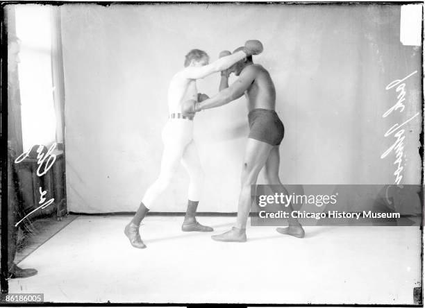 Full-length group portrait of Jack Johnson, African American pugilist, throwing a left jab to the body of pugilist Joe Choynski, standing in front of...