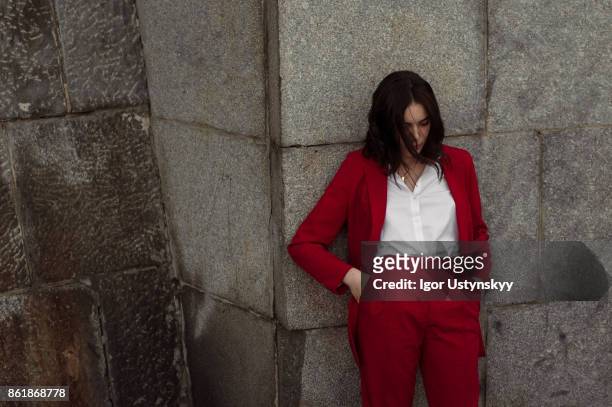 woman in red pantsuit standing near the brick wall - fashion oddities fotografías e imágenes de stock