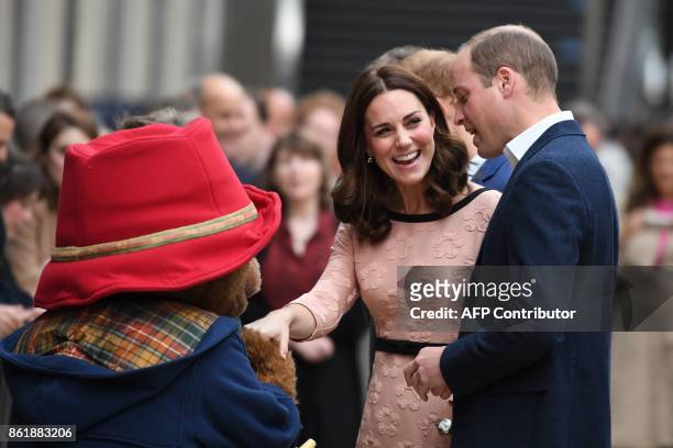 Britain's Catherine, Duchess of Cambridge, laughs as she shakes hands with a person in a Paddington Bear outfit along with her husband Britain's...