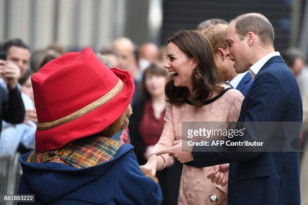 Britain's Catherine, Duchess of Cambridge, laughs as she shakes hands with a person in a Paddington Bear outfit along with her husband Britain's...