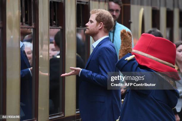 Person in a Paddington Bear outfit and Britain's Prince Harry look through the windows of a Pullman train as they attend a charities forum event at...