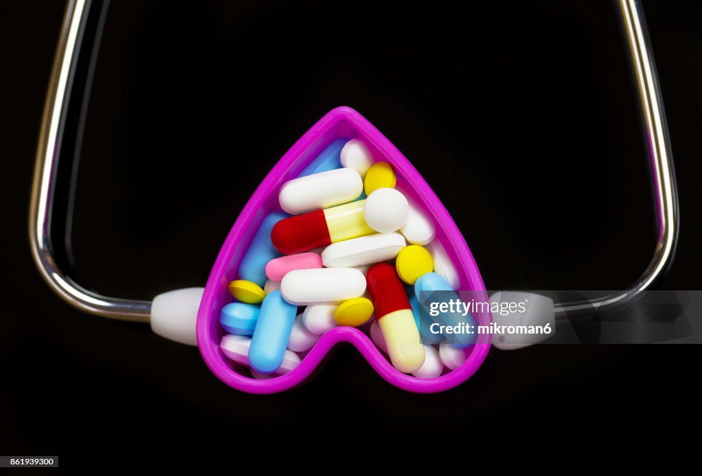 Stethoscope, Capsules and pills in Heart-shaped Container On black background. Medical concept