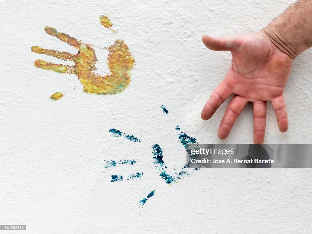 Hands Prints On Wall with colors, on a white wall in the street and the contrast of the open hand of a man