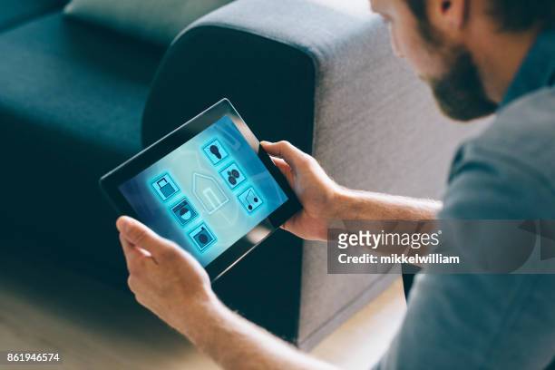 man use smart home automation in living room with digital tablet and mobile app - smart homes stock pictures, royalty-free photos & images