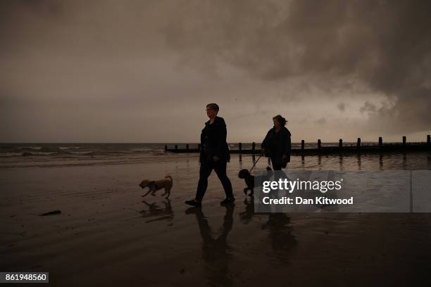 Two women walk their dogs on the beach as storm clouds turn the sky black over the sea front on October 16, 2017 in Bognor Regis, England. The West...