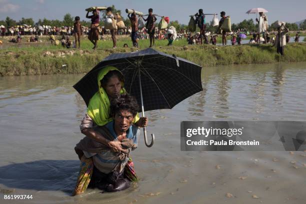 Thousands of Rohingya refugees fleeing from Myanmar cross a small stream in the hot sun on a muddy rice field on October 16, 2017 near Palang Khali,...