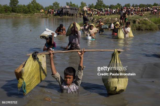 Thousands of Rohingya refugees fleeing from Myanmar cross a small stream in the hot sun on a muddy rice field on October 16, 2017 near Palang Khali,...