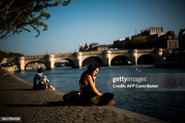 Woman phones as she enjoys a sunny day on the Seine river bank on October 16, 2017 in Paris. / AFP PHOTO / Lionel BONAVENTURE