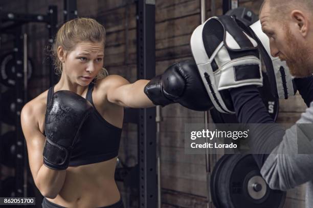 middle aged redhead handsome personal trainer and beautiful young female athlete in gym setting - boxing training stock pictures, royalty-free photos & images