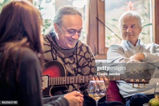 senior hombre cantando y tocando la guitarra para sus amigos - party friends home guitar singers fotografías e imágenes de stock