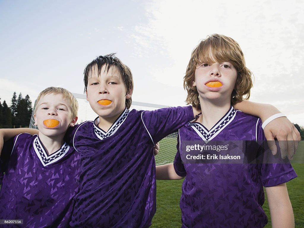 Portrait of boys in soccer uniforms with orange wedges in mouth