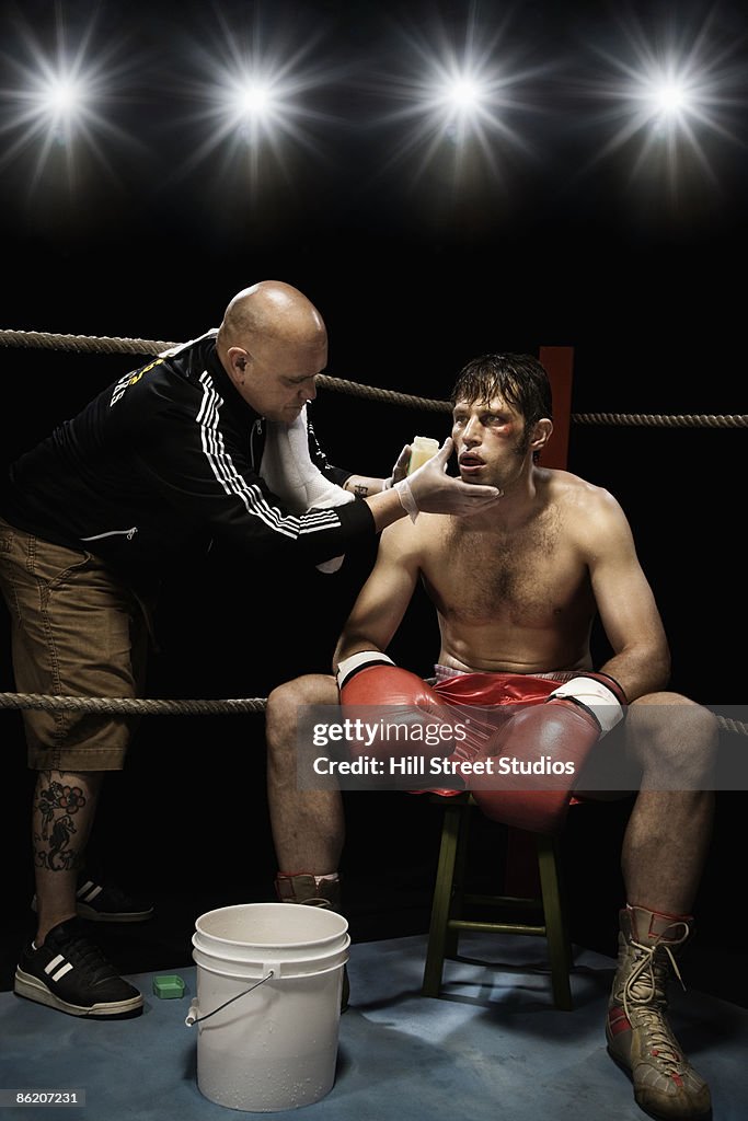 Coach wiping boxer with sponge in corner of boxing ring