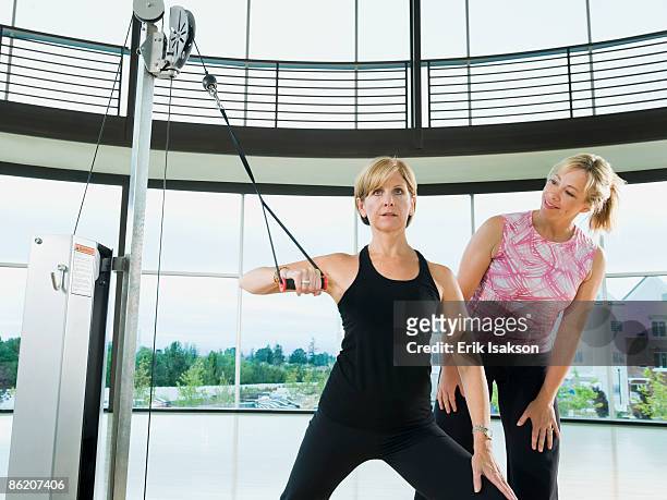 personal trainer standing behind woman exercising - pulley stock pictures, royalty-free photos & images