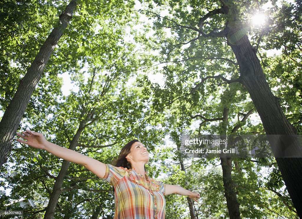 Woman standing below trees with arms outstretched