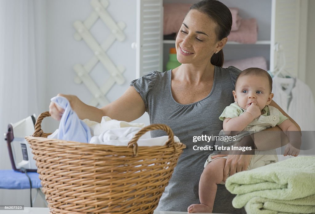 Mother holding baby son and sorting laundry