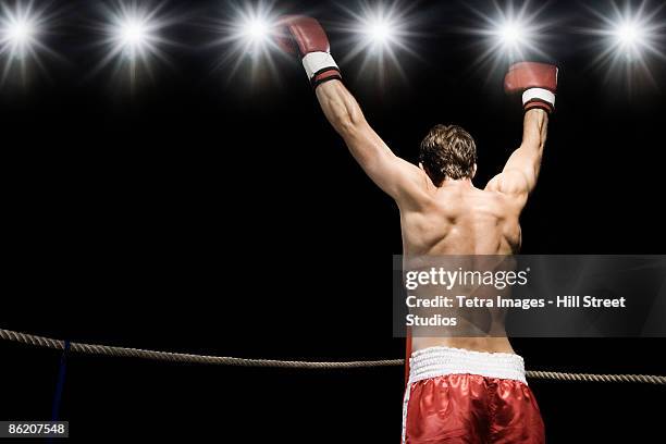 boxer standing in boxing ring with gloves raised - boxing winner stock pictures, royalty-free photos & images