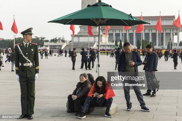 Visitors use their smartphones while a member of the Chinese People's Liberation Army stands guard at Tiananmen Square in Beijing, China on Monday,...