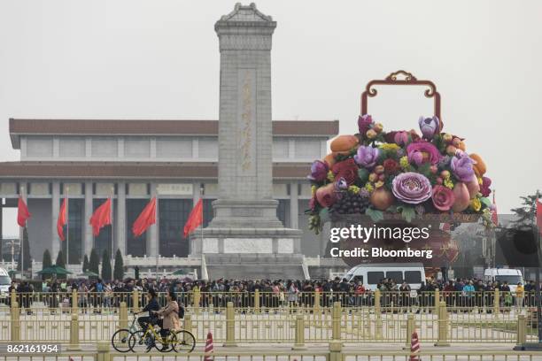 Cyclists ride past a giant bouquet celebrating the 19th congress of the Chinese Communist Party at Tiananmen Square in Beijing, China on Monday, Oct...