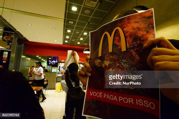 Protesters wave placards and leaflets during an animal rights march outsideand inside McDonald's restaurant on São Paulo on October 17, 2017....