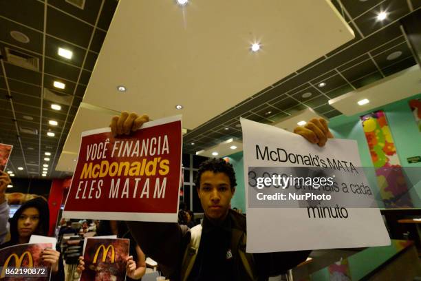 Protesters wave placards and leaflets during an animal rights march outsideand inside McDonald's restaurant on São Paulo on October 17, 2017....