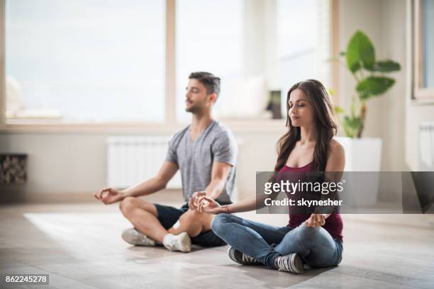 young couple meditating in lotus position in their new apartment. - yoga stock pictures, royalty-free photos & images