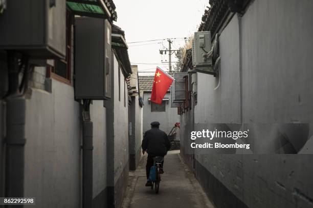 Chinese flag hangs outside a window as a man rides on a bicycle through an alley in Beijing, China, on Tuesday, Oct. 17, 2017. President Xi Jinping...