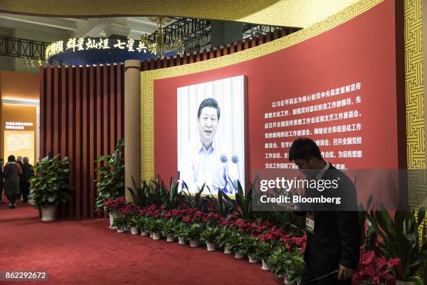 An exhibition worker uses his smartphone while standing next to a photograph of Chinese President Xi Jinping on display at the "Five Years of Sheer...