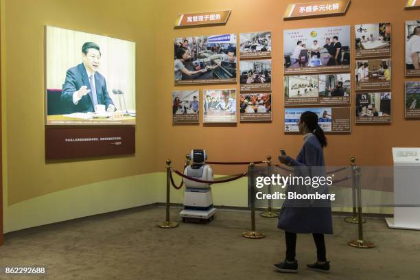 Visitor walks past a surveillance and patrol robot standing in front of a photograph of Chinese President Xi Jinping on display at the "Five Years of...