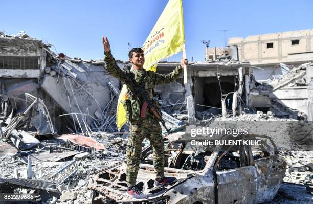 Member of the Syrian Democratic Forces , backed by US special forces, holds up their flag at the iconic Al-Naim square in Raqa on October 17, 2017....