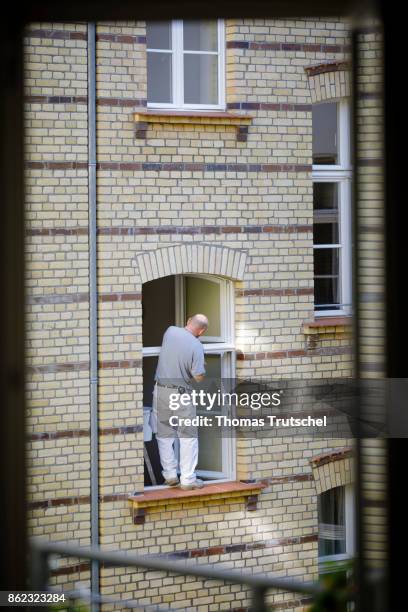Berlin, Germany Symbolic photo on the topic of occupational health and safety. A craftsman stands on a windowsill and repairs a window on October 17,...