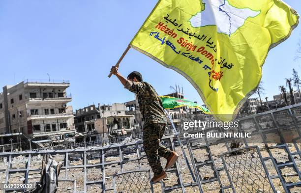 Member of the Syrian Democratic Forces , backed by US special forces, holds up his group's flag at the iconic Al-Naim square in Raqa on October 17,...