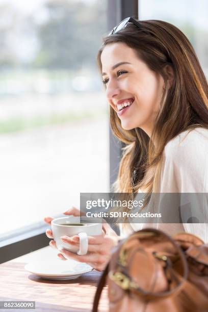 mujer joven alegre mira por la ventana y toma café - célula cultivada fotografías e imágenes de stock