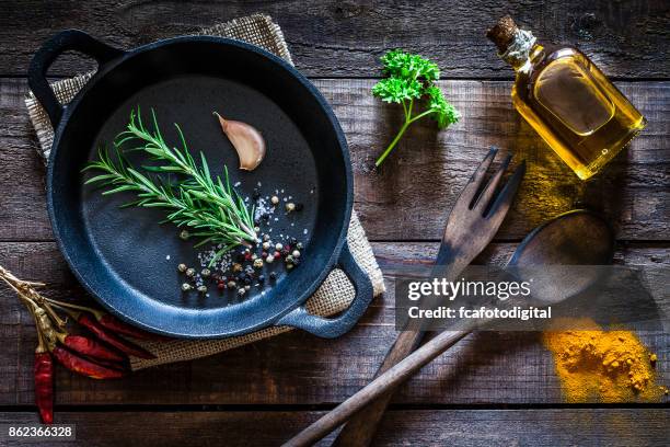 cooking: black cast iron pan with spices and herbs on wooden kitchen table - cast iron stock pictures, royalty-free photos & images