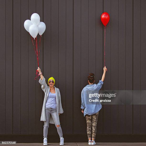 two young women holding balloons while standing against the grey wall - no confidence stock pictures, royalty-free photos & images