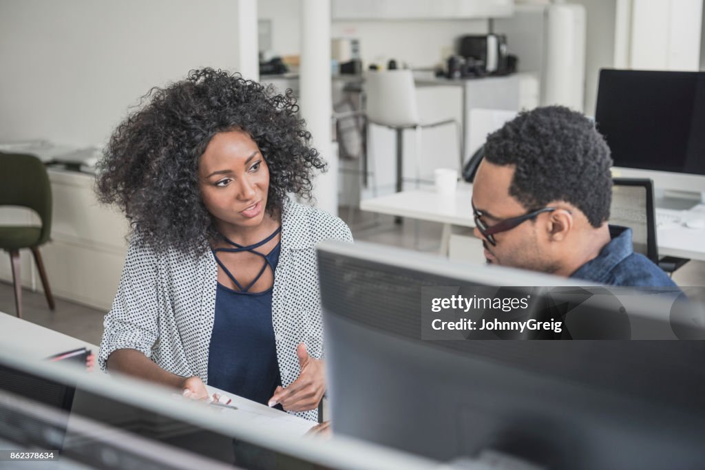 Two business colleagues discussing at desk with woman explaining to man