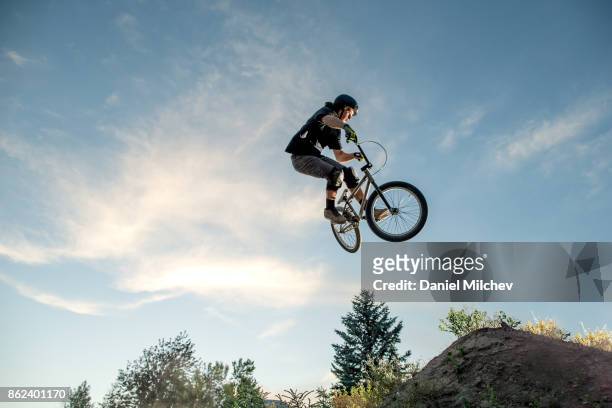 boy with a bmx jumping againds blue sky during sunset. - bmx stock-fotos und bilder