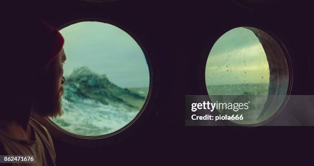 man at the porthole window of a vessel in a rough sea - porthole stock pictures, royalty-free photos & images
