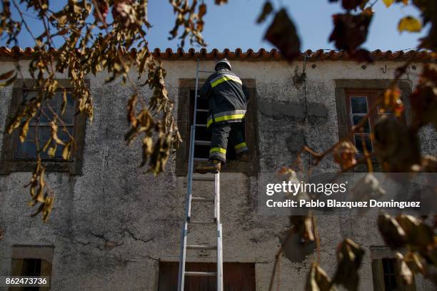 Firefighters enter to a burning house through a window to extinguish the fire in the village of Travanca do Mondego on October 17, 2017 in Coimbra...