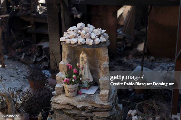 Figure of depicting the Virgin Mary stands at the entrance of a burnt house where a one woman died during a wildfire in the village of Travanca do...