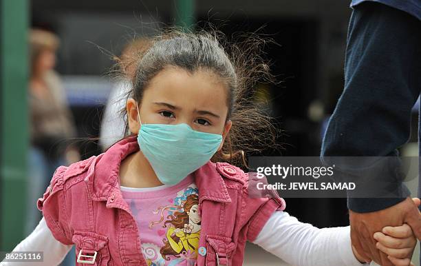 Girl, wearing a mask, holds her father's hand as they cross the international border between US and Mexico in San Ysidro, California, on April 27,...